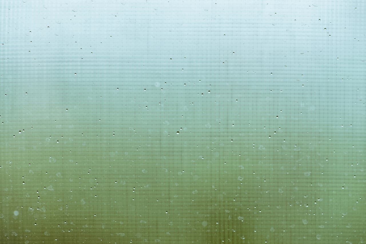 Raindrops on glass with a green gradient background. - Hard Water Etching vs Surface Dirt When Cleaning Isn't Enough